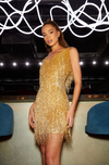 woman stood wearing Sadie gold dress with white lights above