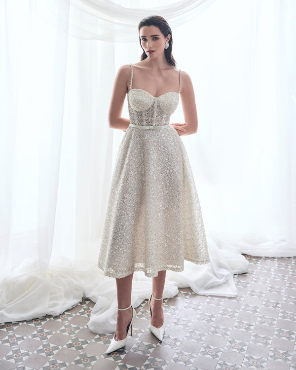 Woman wearing a sparkly silver dress in a white room with draped fabric.