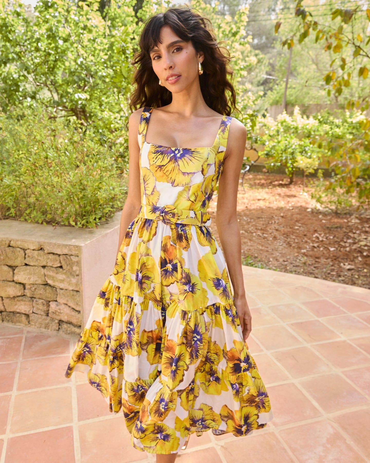 Woman wearing a yellow floral dress standing outdoors with greenery in the background