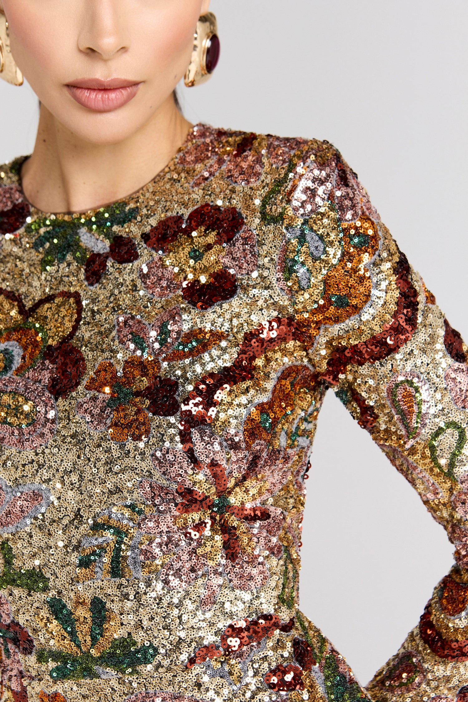 Close-up of a person wearing a sequin dress with floral patterns on a plain background