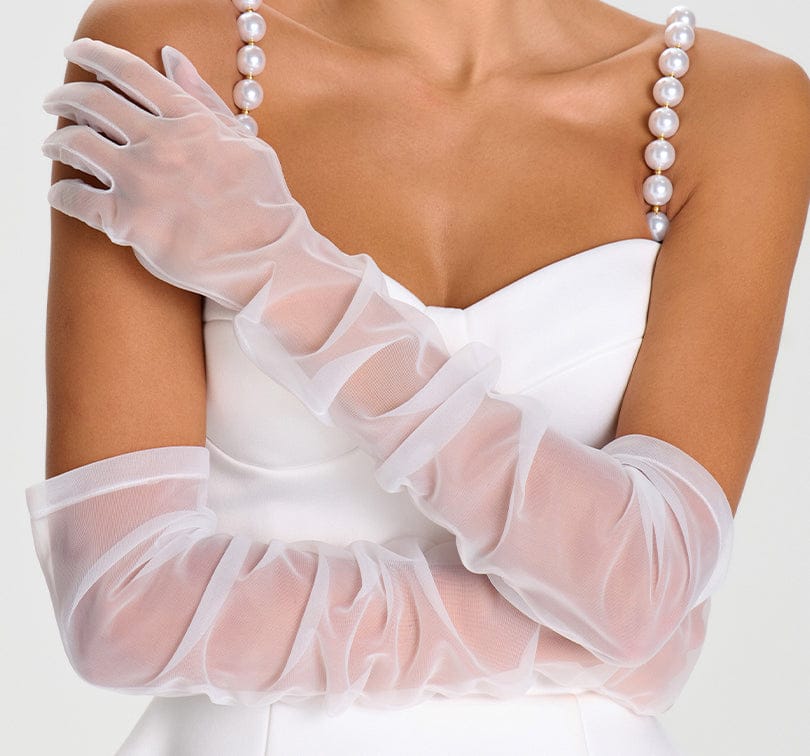 White wedding dress with sheer gloves and pearl necklace on a plain background