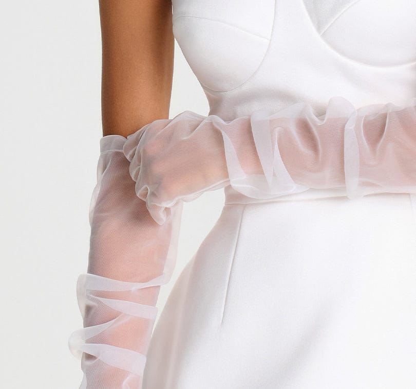Close-up of a white dress with sheer ruffled sleeves on a light background