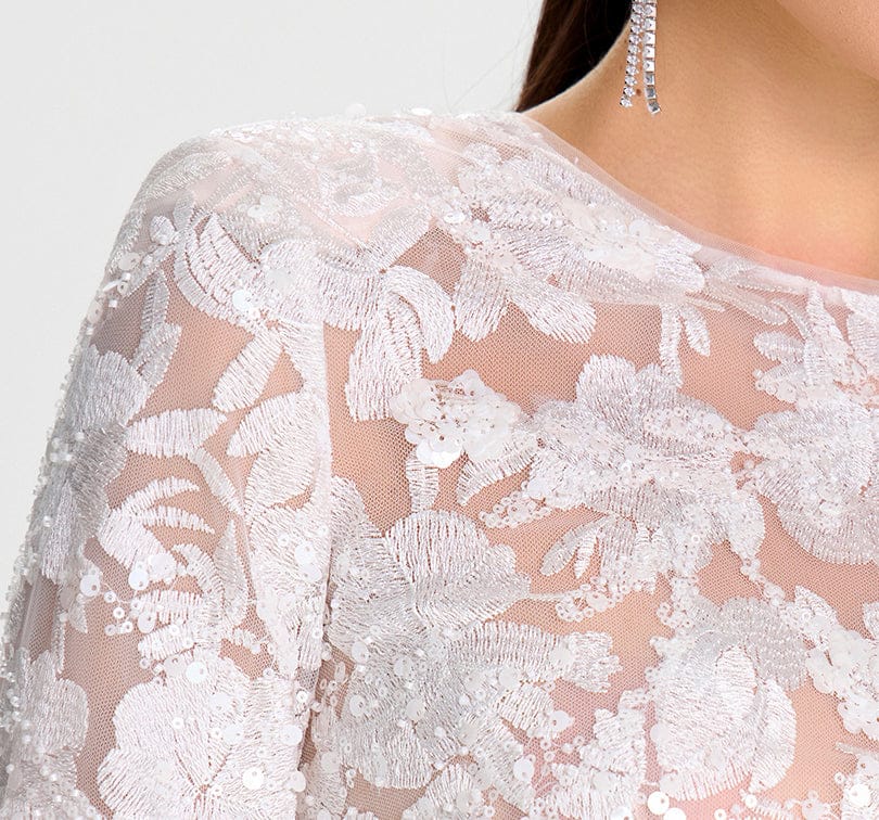 Close-up of a white lace garment with floral patterns on a plain background