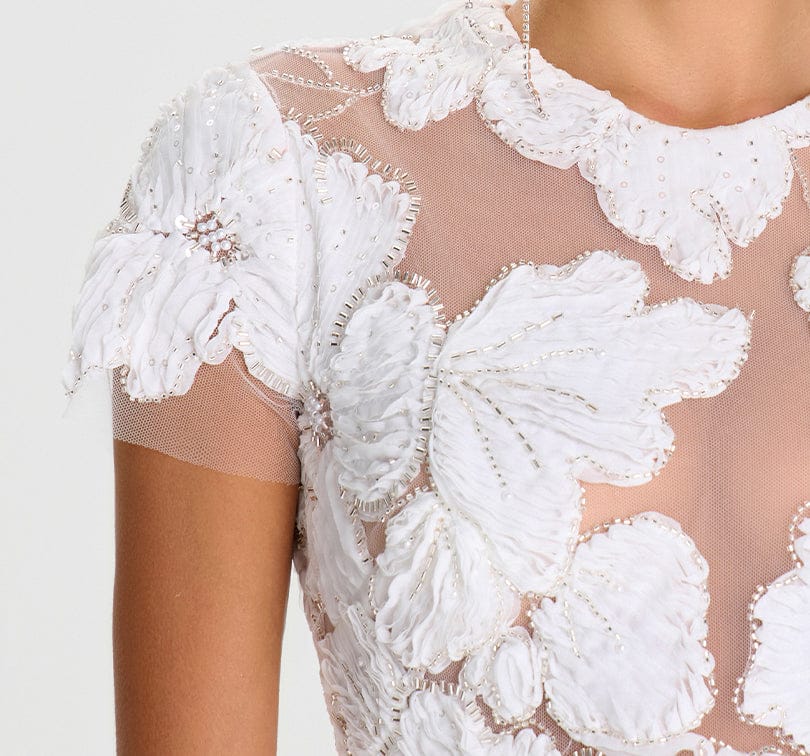 Close-up of a white lace dress with floral patterns on a light gray background