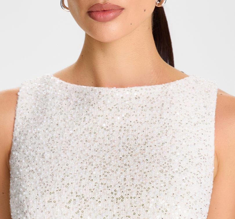 Close-up of a person wearing a white beaded top against a neutral background