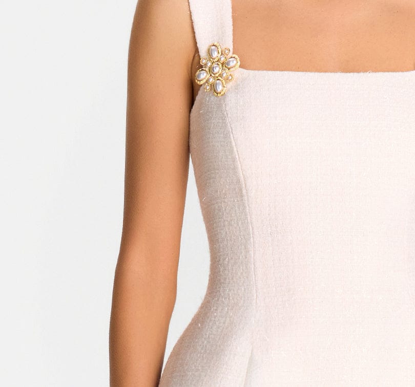 Close-up of a white strapless dress with a decorative brooch on a plain background