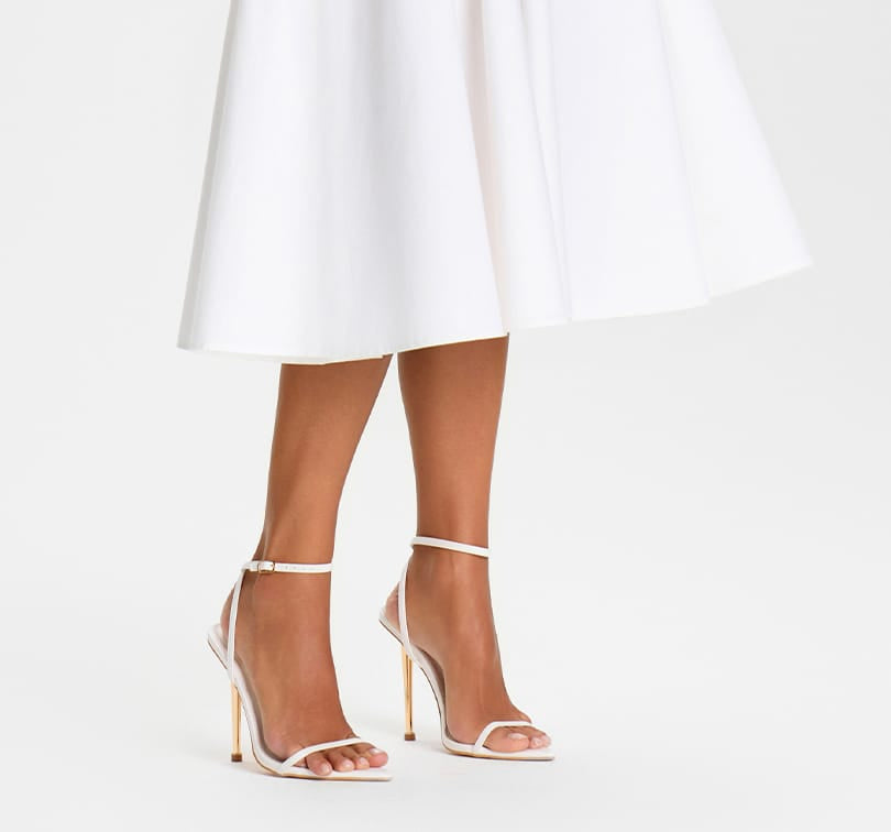 White high-heeled sandals worn with a white skirt on a white background