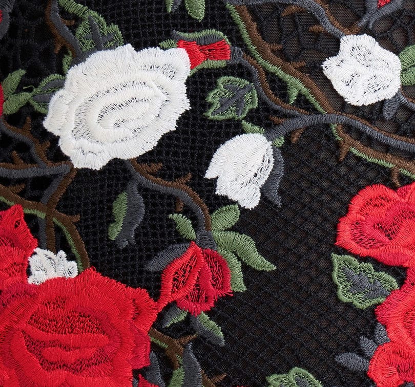 Close-up of embroidered red, white, and green floral patterns on black fabric.