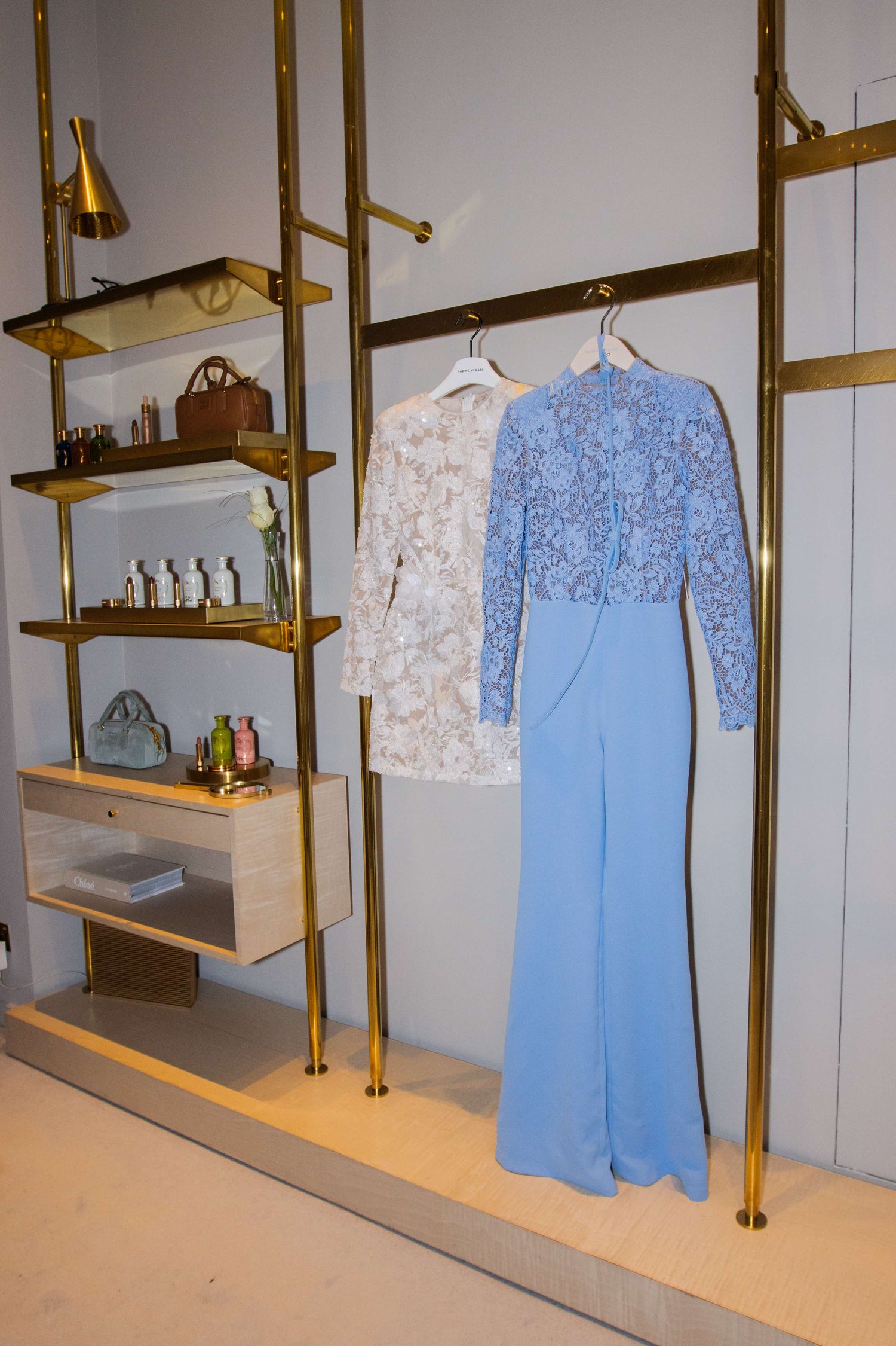 Display of a blue dress and white jacket on a gold rack with shelves.